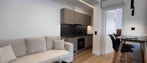 Una cocina moderna con horno empotrado, un comedor con mesa y sillas, y una sala de estar con sofá y mesa de centro.