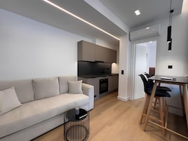 Una cocina moderna con horno empotrado, un comedor con mesa y sillas, y una sala de estar con sofá y mesa de centro.