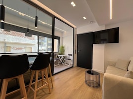Una sala de estar moderna con un sofá, un televisor en la pared y un comedor con sillas y una mesa.