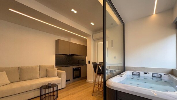 A modern living room with a sofa, a coffee table, a kitchen area, and a hot tub. - BlueMotion - CruiseNest Single  (Piraeus)