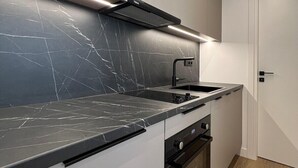 A modern kitchen with a black marble countertop, a built-in oven, and a sleek black range hood. - BlueMotion - CruiseNest Single  (Piraeus)