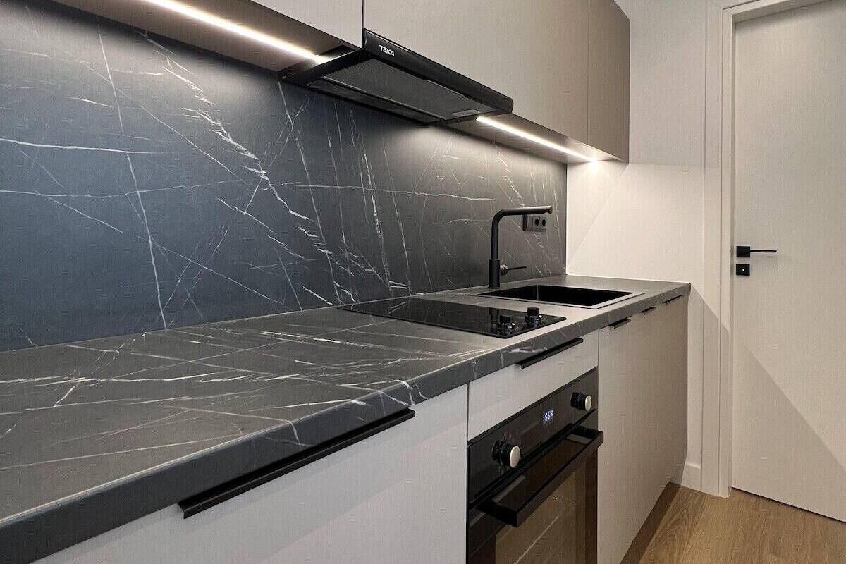 A modern kitchen with a black marble countertop, a built-in oven, and a sleek black range hood.