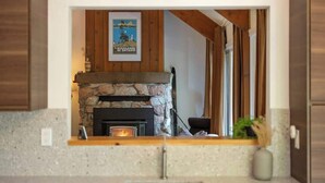 A kitchen with a stone fireplace, wooden beams, and a framed poster on the wall.
