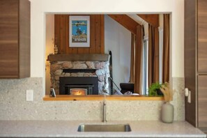 A kitchen with a stone fireplace, wooden beams, and a framed poster on the wall.