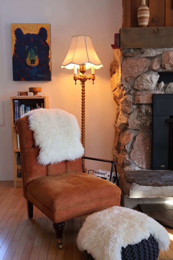 A cozy living room with a wooden chair, a lamp, a bookshelf, and a stone fireplace.