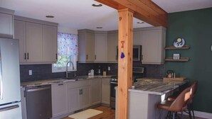 A kitchen with light gray cabinets, a wooden island with bar stools, a dishwasher, and a microwave. - Mountain View Chalet (Calabogie)