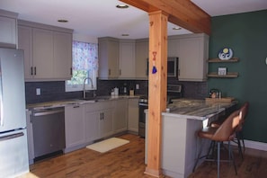 Una cocina con armarios grises claros, una isla de madera con taburetes de bar, un lavavajillas y un microondas.