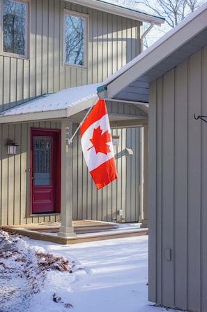 Una casa con puerta roja, un porche y una bandera canadiense.
