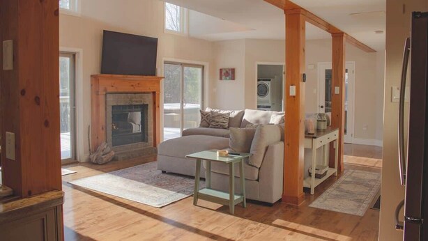 A living room with a fireplace, a sofa, a television, and a kitchen area with a refrigerator. - Mountain View Chalet (Calabogie)
