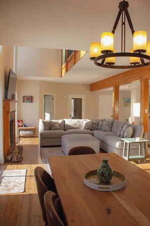 A spacious living area with a large L-shaped sofa, a wooden dining table, and a chandelier.