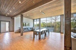 A spacious room with a wooden ceiling, large windows, a dining area with a table and chairs, and a seating area with a sofa and cushions.