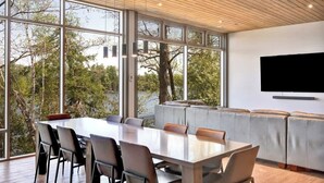 A modern dining area with a large table and chairs, a seating area with cushioned benches, and a television mounted on the wall. - Lake House Wood Sauna & Hot Tub (Portland)