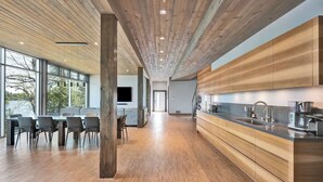 A modern kitchen with wooden cabinetry, a large island with a sink, and a dining area with chairs. - Lake House Wood Sauna & Hot Tub (Portland)