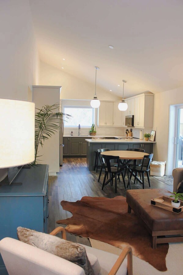 A modern kitchen with a central island, pendant lighting, and a dining area with chairs.