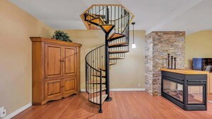 A spiral staircase with a wooden finish and black railings, a wooden cabinet, a stone wall, and a fireplace with a black frame. - KilDrummy Cottage with Sauna (Calabogie)