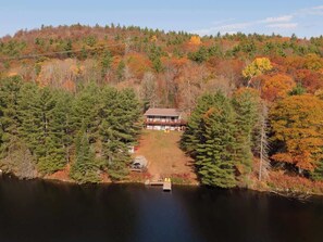 A lodge surrounded by a forest with a lake in front.