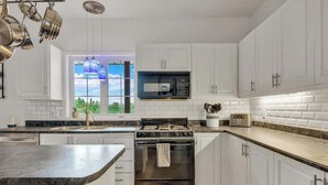 A modern kitchen with white cabinets, a black stove, a microwave, and a window with a view of greenery. - KilDrummy Cottage with Sauna (Calabogie)
