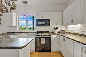 A modern kitchen with white cabinets, a black stove, a microwave, and a window with a view of greenery.