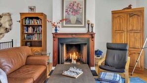 A living room with a fireplace, a bookshelf, a leather sofa, a chair, and a chessboard. - KilDrummy Cottage with Sauna (Calabogie)