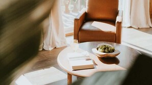 A room with a large window, a chair, a table with a bowl of food, and a book.