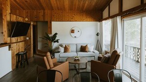 A cozy room with a wooden ceiling, a light-colored sofa, a round coffee table, and a television mounted on the wall.