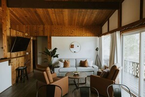 Une pièce chaleureuse avec un plafond en bois, un canapé de couleur claire, une table basse ronde et un téléviseur fixé au mur.