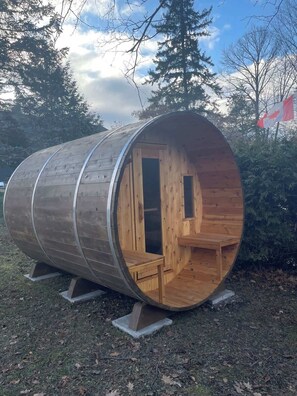 Une structure cylindrique en bois, dotée d’une porte, de fenêtres et d’un banc à l’intérieur.