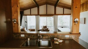 A kitchen with a wooden ceiling, a sink, and a view of a balcony with a chair and a table.