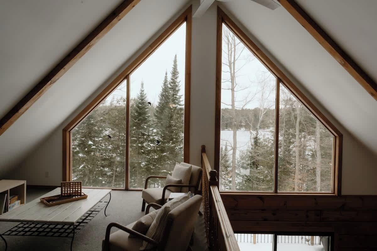 A room with a sloped ceiling, large windows, a wooden bench, and a table with a tray.