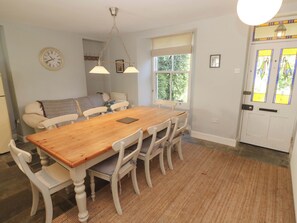 A dining area with a wooden table and white chairs, a clock on the wall, and a window with curtains. - Pedn Brose (Penzance)