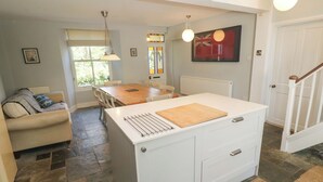 Een keuken met een centraal eiland, een eettafel, een bank en een trap.