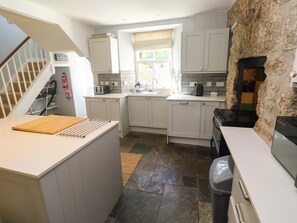 A kitchen with white cabinets, a stone wall, a window with blinds, a toaster, and a stove. - Pedn Brose (Penzance)