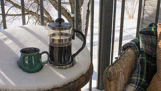 Un tavolo di legno con una caffettiera e una tazza su un terrazza circondata dalla neve.