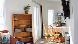Un soggiorno con divano, una libreria in legno, un'area pranzo con tavolo e sedie, e una TV a parete.