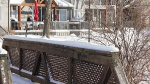 Un ponte di legno coperto di neve con una ringhiera, che conduce a un edificio con diverse finestre e un portico.