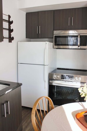 Una cocina compacta con armarios oscuros, un refrigerador blanco, un microondas de acero inoxidable y un horno.