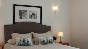 Un letto rifatto con cura, una lampada da comodino e due quadri appesi alla parete.