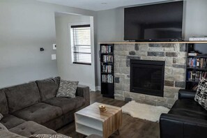 A living room with a stone fireplace, a flat-screen TV, and a bookshelf.