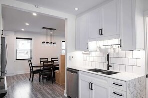 A modern kitchen with white cabinets, a dishwasher, and a dining area with a table and chairs.