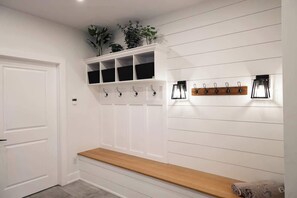 A hallway with a bench, a coat rack, and a shelf with plants.