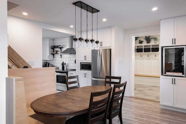 A modern kitchen with white cabinets, a stainless steel refrigerator, and a wooden dining table.