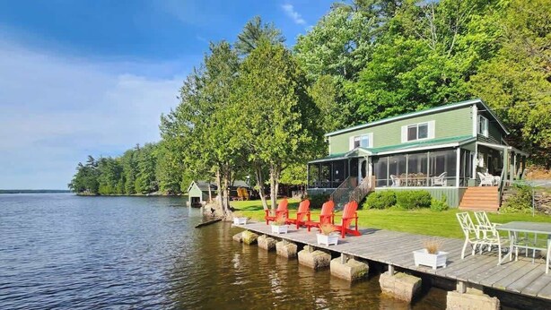 A lakeside property with a dock, outdoor seating, and a house with a green roof. - Loggers Lodge an Anglers Retreat (Calabogie)
