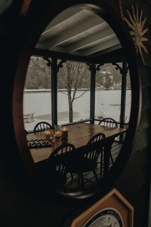 Un espacio de estar al aire libre cubierto, con una mesa, sillas, un reloj y vistas a un paisaje nevado.