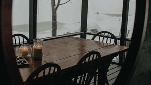 A covered outdoor dining area with a table and chairs, a candle, and a view of a snowy landscape. - Loggers Lodge an Anglers Retreat (Calabogie)