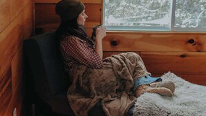 A person sitting by a window in a wooden cabin with a blanket and a teddy bear. - Loggers Lodge an Anglers Retreat (Calabogie)