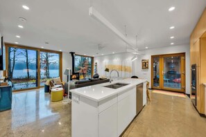 A modern kitchen with a central island, large windows, and a view of the outdoors.