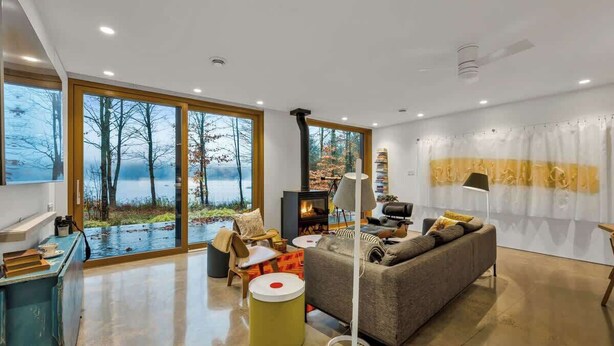 Ein modernes Wohnzimmer mit Kamin, großen Fenstern und Blick auf Bäume.