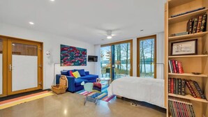 Ein modernes Schlafzimmer mit einem Bett, einem blauen Sofa, einem Bücherregal und einem großen Fenster.