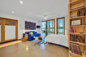 A modern bedroom with a bed, a blue sofa, a bookshelf, and a large window.