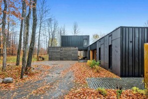 Un bâtiment moderne doté d’un toit plat, d’une allée pavée et entouré d’une zone boisée.